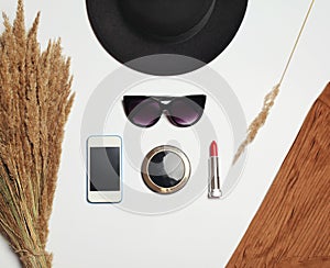 Fashion accessory, round black hat, sunglasses, screen smartphone, mirror and red lipstick on white background