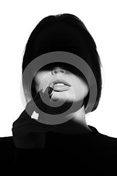 Fashion advertising portrait of a young beautiful girl using lipstick. Black and white silhouette with epic light.