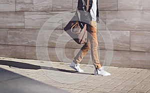 Fashion african man in black rock leather jacket with bag walking over grey textured at evening city