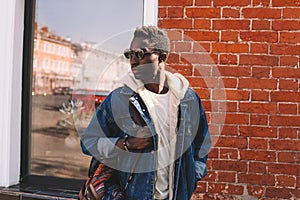 Fashion african man in jeans jacket, with backpack walking on city street