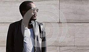 Fashion african man wearing a sunglasses and black rock leather jacket over textured background evening in city