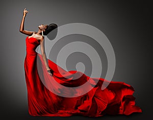 Fashion African Woman in Silk Dress dancing. Dark Skinned Model with Black Afro Hair in Long Evening Red Gown with Tail Fabric