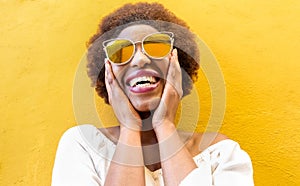 Fashion african woman smiling and wearing sunglasses with yellow ochre background - Black afro girl having fun - Focus on face -