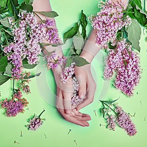 Fashion art hands natural cosmetics women, bright purple lilac flowers in hand with bright contrast makeup, hand care. Creative