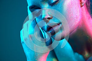 Fashion art. Model girl in colorful bright sparkles and neon lights posing in studio, portrait of beautiful woman