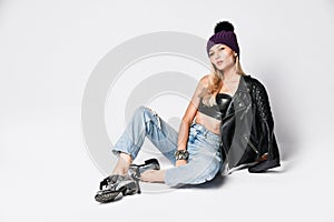 Fashion art photo of grunge style girl in blue torn jeans, leather bralet, jacket with zippers, boots and winter hat