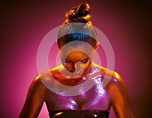 Fashion art portrait. Model girl in colorful bright sparkles, gold and pink skin, neon lights  posing in studio, beautiful woman