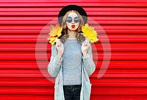 Fashion autumn portrait woman with yellow maple leaves on a red