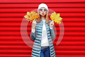 Fashion autumn woman holds yellow maple leaves on a red