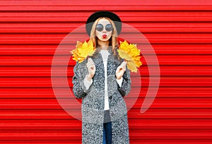 Fashion autumn young woman with red lips holds yellow maple leaves