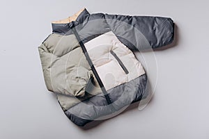 Fashion baby colorblock puffer jacket on grey background. Top view, flat lay. Newborn beige clothes outfit. Winter