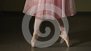 Fashion ballerina dancing in a dark ballet class. The girl performs dance steps in a stage costume. Slow motion.