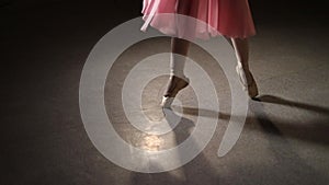 Fashion ballerina dancing in a dark ballet class. The girl performs dance steps in a stage costume. Slow motion.