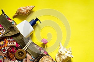 Fashion beach accessories - bag, suntan lotion, seashells and sunscreen on a yellow background