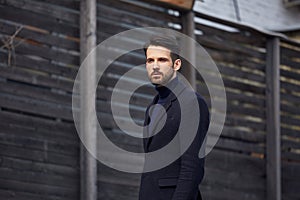 Fashion beard style business handsome male model posing in style clothing blue jacket and trousers on street wooden wall outdoors