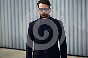 Fashion beard style business handsome man posing in style clothing and trendy sun glasses on street wall outdoors background.