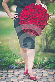 Fashion beautiful woman is wearing black dress is holding big bouquet of 101 red roses