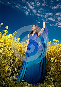 Fashion beautiful young woman in blue dress posing outdoor with cloudy dramatic sky in background. Attractive long hair brunette