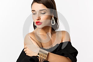 Fashion and beauty concept. Elegant woman with red lips, black dress, showing earrings and jewelry, white background