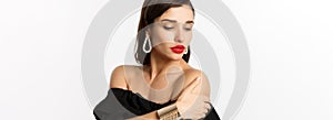 Fashion and beauty concept. Elegant woman with red lips, black dress, showing earrings and jewelry, white background