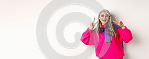 Fashion and beauty concept. Image of stylish asian senior woman in sunglasses smiling, showing peace signs and looking