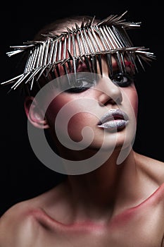 Fashion beauty model with metallic headwear and shiny silver red makeup and blue eyes and red eyebrows on black background