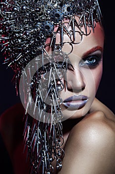 Fashion beauty model with metallic headwear and shiny silver red makeup and blue eyes and red eyebrows on black background