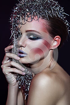 Fashion beauty model with metallic headwear and shiny silver red makeup and blue eyes and red eyebrows on black background