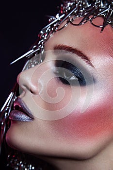 Fashion beauty model with metallic headwear and shiny silver red makeup and blue eyes and red eyebrows on black background