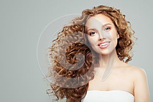 Fashion beauty portrait of young redhead woman with long healthy curly hair gray background
