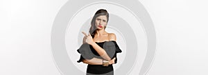 Fashion and beauty. Skeptical glamour woman with red lips, black dress, pointing finger right at something lame and