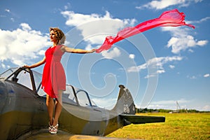 Fashion beautyful woman in red dress stays on a wing of the old plane