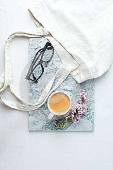 Fashion blog marble style desk with woman accessory: cup of coffee, lilac branches. googles and zero waste tissue bag on white