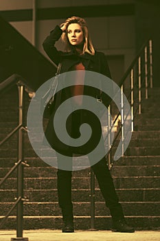 Fashion blond business woman in black coat standing on steps at office building