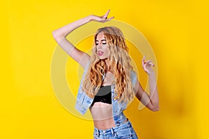 Fashion blonde model with wavy long hair and glamour makeup in summer look, posing over yellow background.