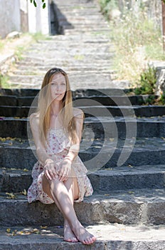 Fashion blonde wearing flower dress sitting on stone stairs