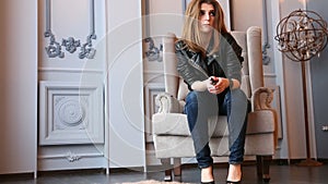 fashion brown hair woman sitting on luxury armchair leather jacket and denim jeans.