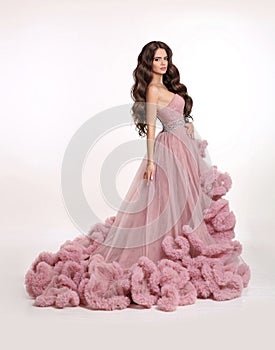 Fashion brunette woman in gorgeous long pink dress posing isolated on white studio background. Beautiful Lady in luxury lush gown.