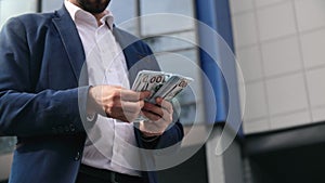 Fashion business man in suit counting cash money dollar profit outdoor downtown office closeup