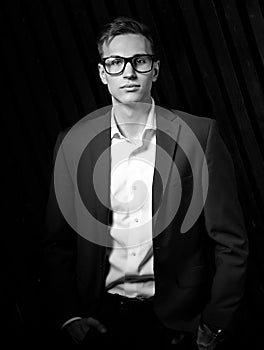 Fashion business man in suit posing in trendy eyeglasses on black studio dark background. Elegant portrait. Black and white