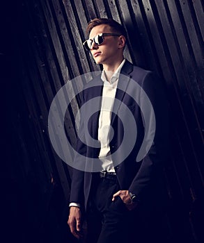 Fashion business man in suit posing in trendy eyeglasses on black studio wooden background. Closeup toned vintage elegant portrait