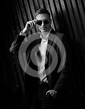 Fashion business man in suit posing in trendy eyeglasses on black studio wooden background. Elegant portrait. Black and white