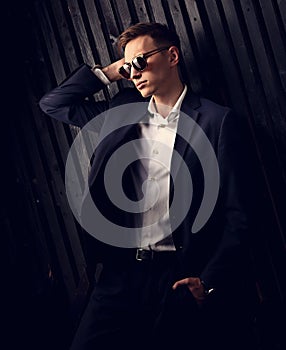 Fashion business man in suit and white shirt posing in trendy eyeglasses on black studio wooden background. Closeup toned elegant