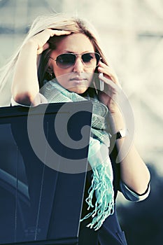 Fashion business woman in sunglasses calling on phone next to car