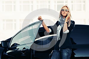 Fashion business woman in sunglasses talking on cell phone beside a her car