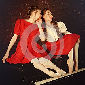 Fashion caucasian ballerinas sitting on the piano and laughing