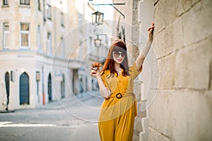 Fashion city portrait of gorgeous young Caucasian red haired woman, dressed in stylish yellow overalls, sunglasses and