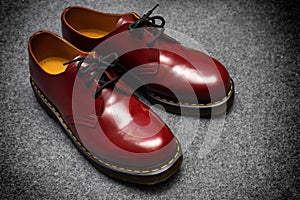 Fashion classical cherry red oxblood men`s leather shoes with black lace on gray carpet.