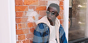 Fashion close-up portrait african man wearing jeans jacket on city street over brick textured wall