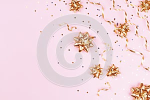 Fashion composition with golden bows, serpentine and star confetti on pink pastel table top view. Flat lay card for christmas.